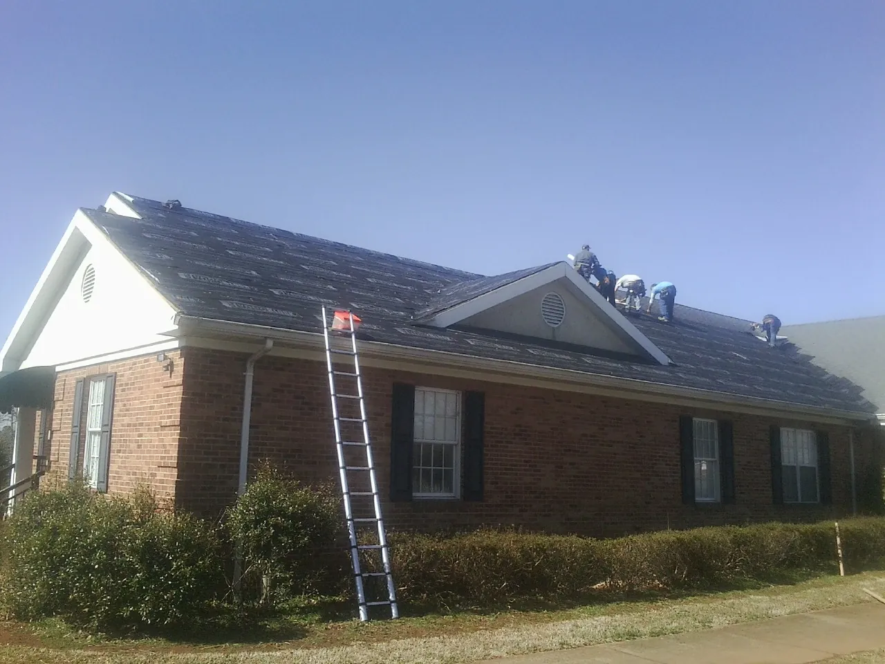 Crew tearing shingles off a brick ranch roof with a ladder set — Emergency Roof Repair work by our crew in Randleman