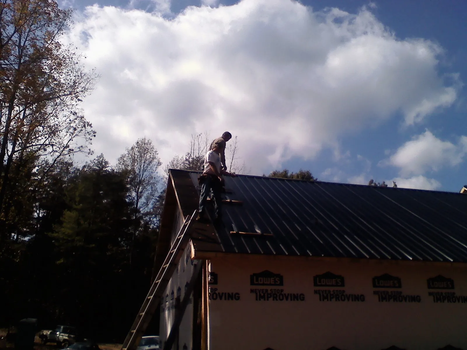Roofer fastening dark metal panels high against a cloudy sky, from a Roof Inspection job in Randleman