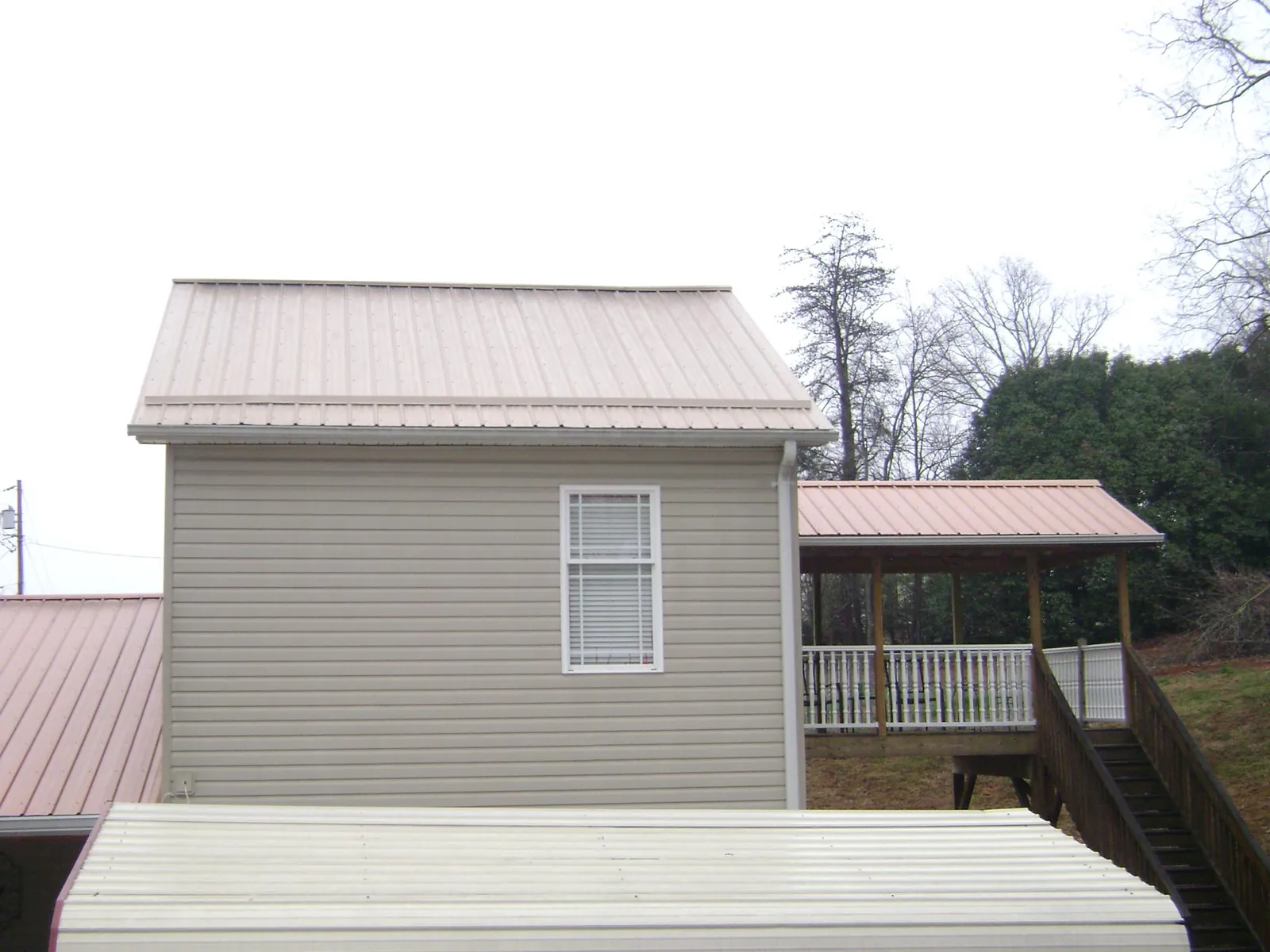 Tan metal roofs on a two story addition and attached porch, from a Roof Replacement job in Randleman